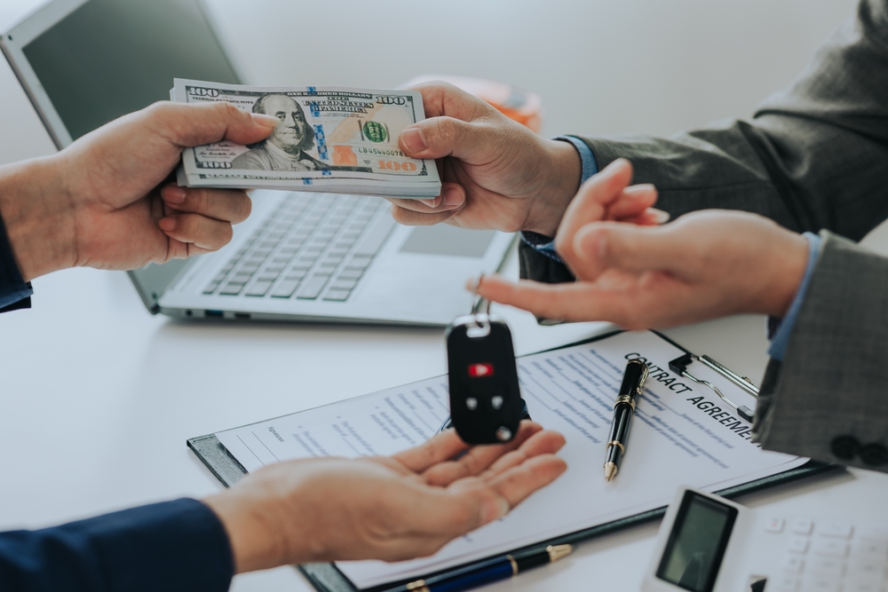Person hands money to another person in exchange for car keys, with a contract agreement on the table